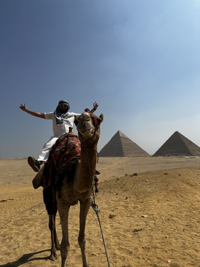 The founder riding a camel in front of the pyramids of Giza, face blurred